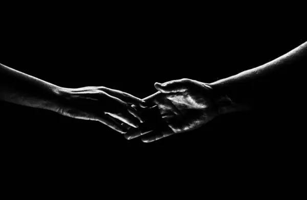 Two hands reaching toward. Helping hand outstretched for salvation on isolated black background. Close up of man and woman hand touch with fingers