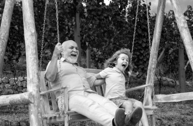 Young grandson and old grandfather swinging in spring garden. Grand dad and grandson sitting on swing in park