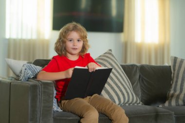 Eğitim kavramı, çocukluk, kitap okuma, sanat eseri, ilham. Çocuk oturma odasında kitap okuyor. Çocuklar kitap okur. Küçük çocuk güneşli oturma odasında kanepede oturuyor.