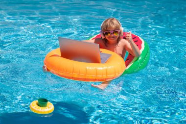 Yaz ofisi ve serbest çalışma konsepti. Çocuk yaz havuzunda dizüstü bilgisayarla çalışıyor. Bilgisayar kullanan, havuz başında çalışan küçük bir serbest çalışan.