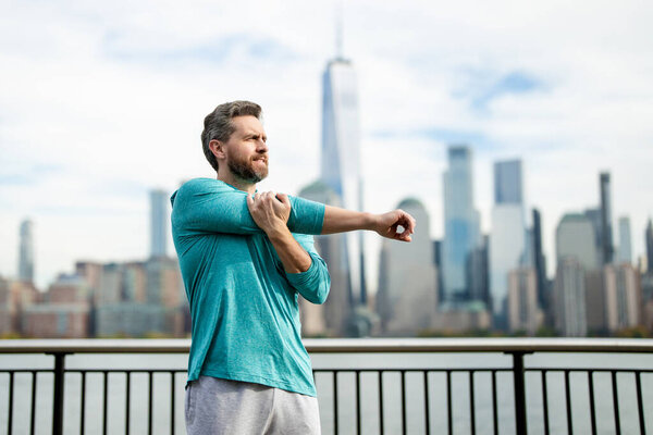 Mature man in sportswear stretching his arms outside. Athletic Mature Fit Man Doing Exercises in City outdoor. Happy man workout in New York city. Sport, fitness and exercise