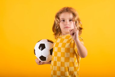 Çocuk çocuk klasik futbol topunu sarı stüdyoda izole bir şekilde tutuyor. Stüdyoda elinde futbol topu tutan çocuk. Çocuk topla oynuyor. Spor, çocuklar için futbol hobisi. Futbol topuyla poz veren küçük bir futbolcu