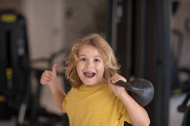 Spor salonundaki çocuk. Dambıllarla egzersiz yapan sevimli küçük çocuk. Kettlebell 'li sportif çocuk portresi. Egzersiz yapan mutlu çocuk. Sağlıklı aktiviteler, çocuk yaşam tarzı