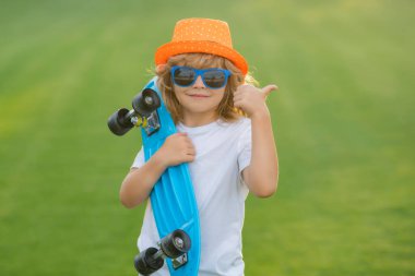 Çocuk pembe arka planda uzun tahta tutuyor. Pennyboard 'u olan çocuk. Bozuk paralı neşeli küçük bir çocuğun açık hava portresi. Yaz çocukları modası