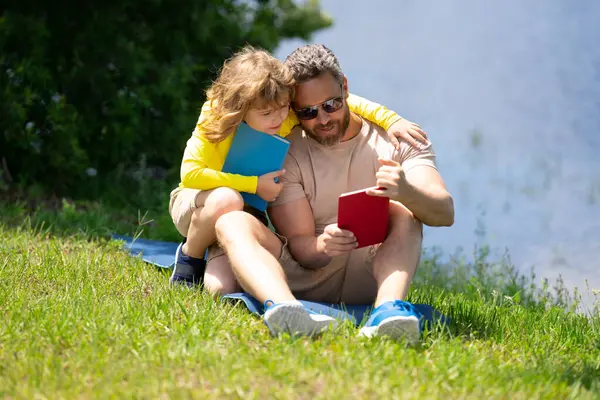 爸爸和儿子在公园里看书 教育和友谊的概念 生活方式 父亲在户外给他可爱的儿子读了一本书 温暖的夏日 家庭关系 孩子和父母 — 图库照片
