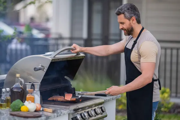 庭のバーベキューグリルで男料理 肉を調理バーベキューグリルで調理します 男はバーベキューで肉を調理夏の家族の夕食のために家の裏庭で — ストック写真