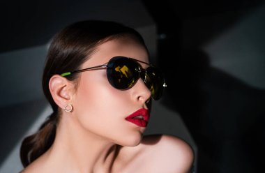 Moda gözlüklü, kırmızı dudaklı şık bir kadın model. Karanlıkta izole edilmiş ciddi bir kadının portresi. Genç bir kadın poz veriyor. Güneş gözlüklü genç bir kadının portresi.