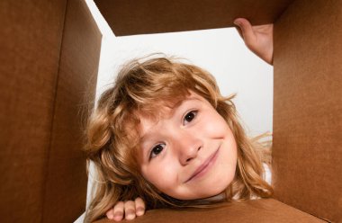 Şaşkın çocuk bavulunu açıyor, kutusunu açıyor ve içine bakıyor. Paket, teslimat, sürpriz, çocuk için hediye. Çocuk duyguları ve çocuk yüz ifadeleri. Yakın çekim çocuk yüzü.