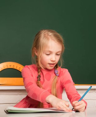 School concept. Kids drawing in notepad. Little girl pupil study in classroom. School student taking notes from book for study