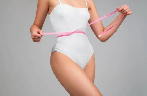 Slim woman with measuring tape around the waist line. Fit fitness girl measuring waistline with measure tape. Slim woman measuring waist after diet. Slim body, perfect waist