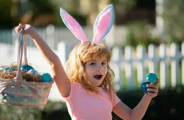 Excited child with easter basket. Child boy hunting easter eggs. Kid with easter eggs and bunny ears outdoor