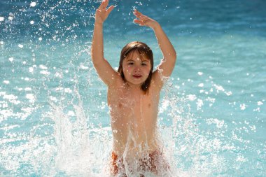 Çocuk yaz havuzunda su sıçratıyor. Çocuk bilardoda su sıçratıyor. Havuza atlayan heyecanlı küçük çocuk, su eğlencesi. Yüzme havuzuna atlayan ve su sıçratan çocuk. Çocuk havuz kenarında su sıçratıyor.