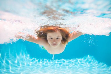 Genç çocuk yüzer ve suyun altına dalardı. Yüzme havuzundaki su altı portresi. Çocuk yüzme havuzuna dalıyor. Çocuklar yaz tatilinde yüzerler.