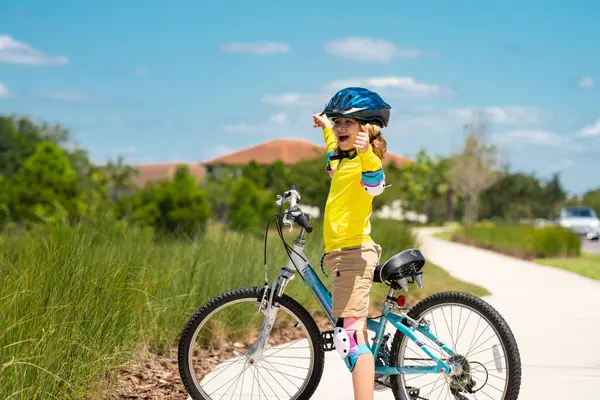 Sporty kid riding bike on a park. Child in safety helmet riding bicycle. Kid learns to ride a bike. Kids on bicycle. Happy child in helmet cycling outdoor. Sports leisure with kids