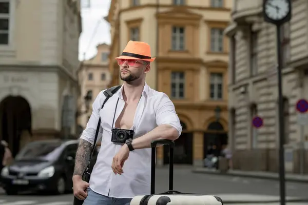 Traveler tourist man in casual clothes hat with suitcase. Handsome young man on business trip walking with his luggage on street. Travelling businessman
