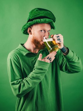 Lucky charms on green background. Leprechauns hat. Man on green background celebrate St Patricks Day. Portrait of excited man holding glass of beer on St Patricks day isolated on green clipart