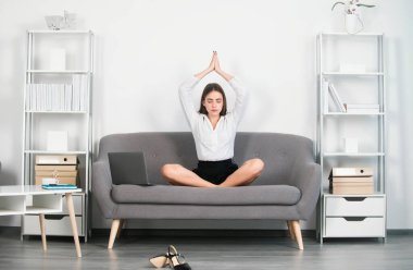 Genç çekici sekreter kadın, modern bir ofiste işyerindeki kanepede yoga egzersizi yapıyor. Ofiste meditasyon yapan güzel bir muhasebeci kız. Çalışanlar denge uyumunu hisseder.