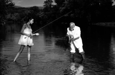 Genç seksi kadın ve yaşlı balıkçı elinde oltayla nehirde duruyor. Baba ve kızı balık tutuyor. Olgun balıkçı emekliliği kutluyor. Balıklı büyükbaba.