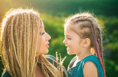 Anne ve kız oynuyorlar ve sarılıyorlar. Saç örüyorum. Örgü ören güzel bir kız çocuğu. Saç örgüsü modaya uygun.