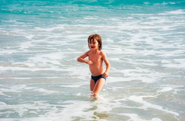 Çocuk yaz tatilinde plajda oynuyor. Doğada çocuklar ve güzel deniz. Mutlu çocuklar deniz kenarında tatildeler, suda koşuyorlar.
