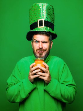 Man in Saint Patricks Day leprechaun party hat hold Pot of gold on green background. Happy St Patricks Day concept with pot of gold clipart
