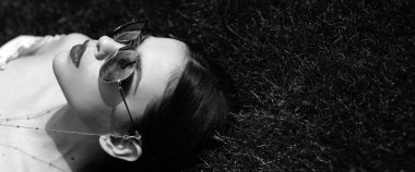 Bahar kadını pankarta karşı. Moda gözlüklü şık bir kadın model. Harika bir teni ve uzun koyu renk saçları olan güzel bir esmer. Çimen arkaplanı