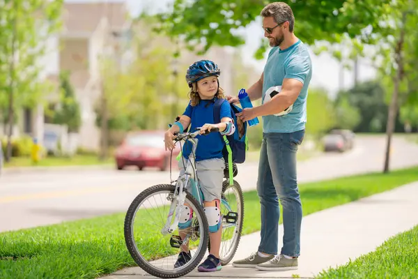 Father teaching son riding bike. Dad helping child son to ride a bicycle in american neighborhood. Child in bike helmet learning to ride cycle with father. Happy fathers day. Summer sport with child