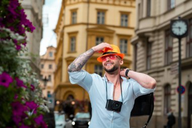 Bagajlı gezgin portresi. Bavullu turist seyahat etmeye hazır. Bavulu açık havada gezen bir erkek. Yaz tatilinde şapka ve güneş gözlüğü takan beyaz bir gencin portresi.