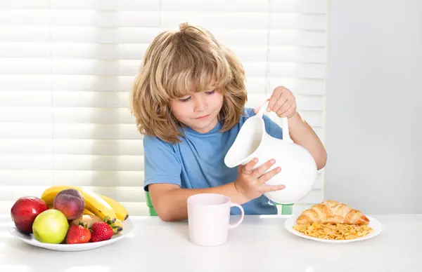 Kid pouring whole cows milk. Kid preteen boy 7, 8, 9 years old eating healthy food vegetables. Breakfast with milk, fruits and vegetables. Child eating during lunch or dinner at home