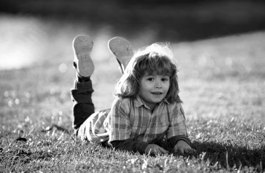 Çocuk dışarıda. Parktaki çocuk. Yay Çocuk çimlerin üzerinde yatıyor. Yaz yürüyüşü. Çocuk adaptasyonu