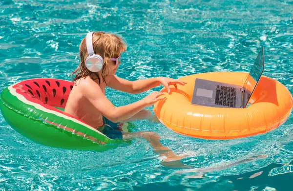 Kids working with laptop on summer vacation holidays. Little freelancer using computer, remote working in swimming pool. Summer business and online technology