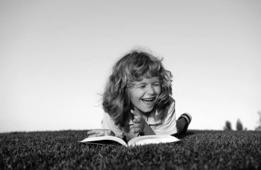 Çocuk kitap okuyor çimlerin üzerinde ve gökyüzü arka planında fotokopi alanı açık havada