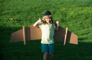 Child boy like a pilot with toy wings against green grass. Kids freedom concept. Dreams of becoming a pilot. Kid pilot with toy jetpack playing outdoors. Happy childhood. Kids dreams. Thumbs up