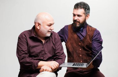 Yetişkin eğitimi. Babasıyla mutlu genç adam dizüstü bilgisayarda komik videolar izlerken eğleniyor. Yaşlı baba ve yetişkin oğul internette internet kullanırken gülümsüyor.