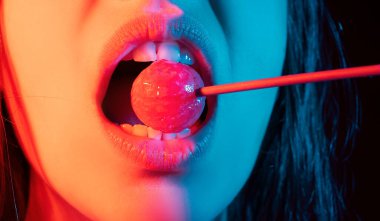 Cazibeli ağız kırmızı dudaklı lezzetli lolipopları yalıyor. Lolipop berbat. Seksi kadın dudağı. Lolipopu olan şehvetli, kırmızı dudaklı bir kadın. Neon ışıklar üzerine çikolata konsepti