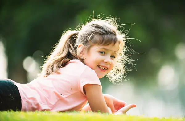 春や夏の芝生の屋外でリラックスして横に幸せな女の子 かわいい子供は公園の芝生に横たわっている — ストック写真