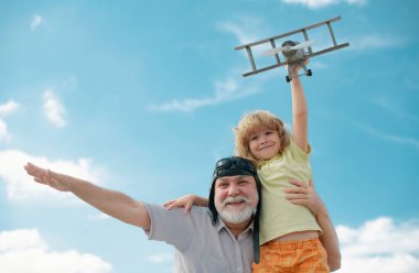 Grandfather and son having fun with plane outdoor on sky background with copy space. Child dreams of flying, happy childhood with granddad. Golden age