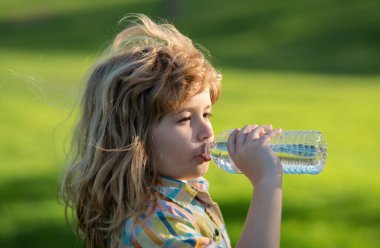 Parktaki evcil hayvan şişesinden su içen çocuk. Çocuk içiyor. Parkta su içen, elinde plastik şişe tutan bir çocuk. Susamış çocuk