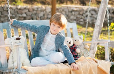 Happy child boy swinging on a swing at the park in summer. Kids happiness and smile. Child playing on outdoor playground. Healthy summer activity for children