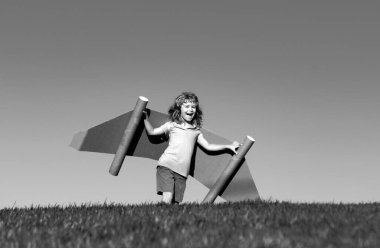 Seyahat hayalleri. Arka planda oyuncak uçakla jetpack üzerinde uçan bir çocuk. Mutlu çocuk karton uçakta oynuyor. Çocuk dışarıda eğleniyor.