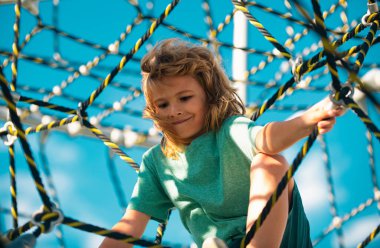 Oyun arka planında kaya tırmanışı yapan sevimli çocuk portresi. Oyun parkında egzersiz yapmak için maymun barında asılı duran küçük çocuk.