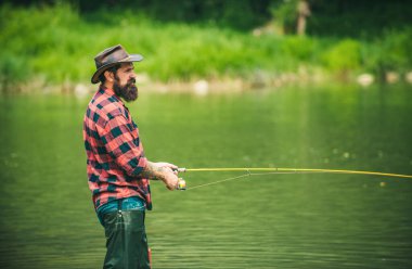 Young bearded man angler fishing at a lake or river. Flyfishing