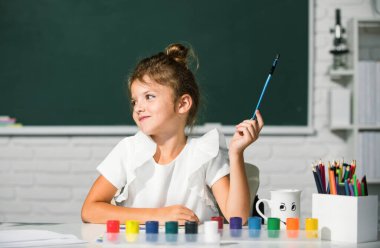 Child girl at school draws with paints. Kids artist creativity. Little funny artist painting, drawing art