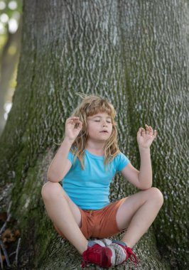 Mudra jestinde parmaklarını tutan ve kapalı gözlerle meditasyon yapan, sakin, olumlu ve doğal arka planda rahat bir çocuk. Çocuklar yoga yapıyor.
