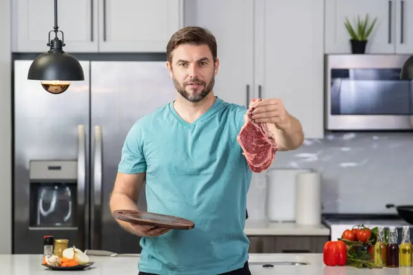 Handsome man cooking meat beef steak in kitchen. Portrait of casual man cooking with meat ingredients. Casual man preparing raw meat in kitchen. Chef cooking beef steak