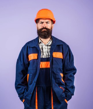 Kasklı, ciddi sakallı bir adam. İnşaat malzemeleri ve kaskı olan çılgın bir miğferci. Şapkalı adam, yenileme konsepti. İnşaatçı ve zor iş. İnşaatçı, müteahhit