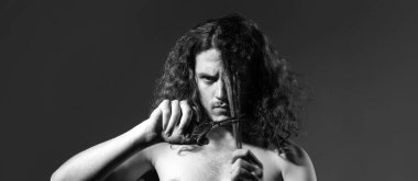Young man, banner of guy with barber scissors for barber shop. Handsome male model long curly hair