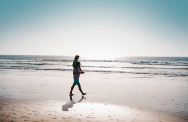 Yakışıklı adam baba, küçük oğlan çocuğu taşıyor. Mutlu baba kucağında çocuğu. Baba ve oğul yaz plajında yürüyor. Çocukluk ve ebeveynlik kavramı