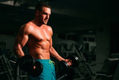 Spor salonunda pazı kaldıran bir sporcu. Çıplak gövdeli genç kaslı adam spor salonunda çalışıyor. Spor yapan atletik erkek sporcu. Spor konsepti