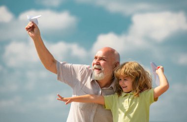 Mavi gökyüzü ve bulutların üzerinde kağıt uçakla uçan çocuk ve büyükbaba. Erkek nesli büyükbaba ve torun. Yaşlı bir akraba ve çocuk.